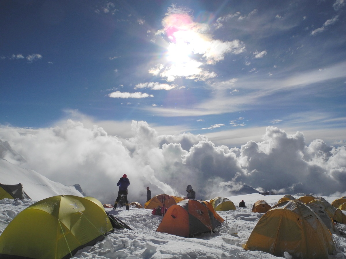 Cluster of yellow and orange tents in a snowy mountain climbing camp shrouded by clouds