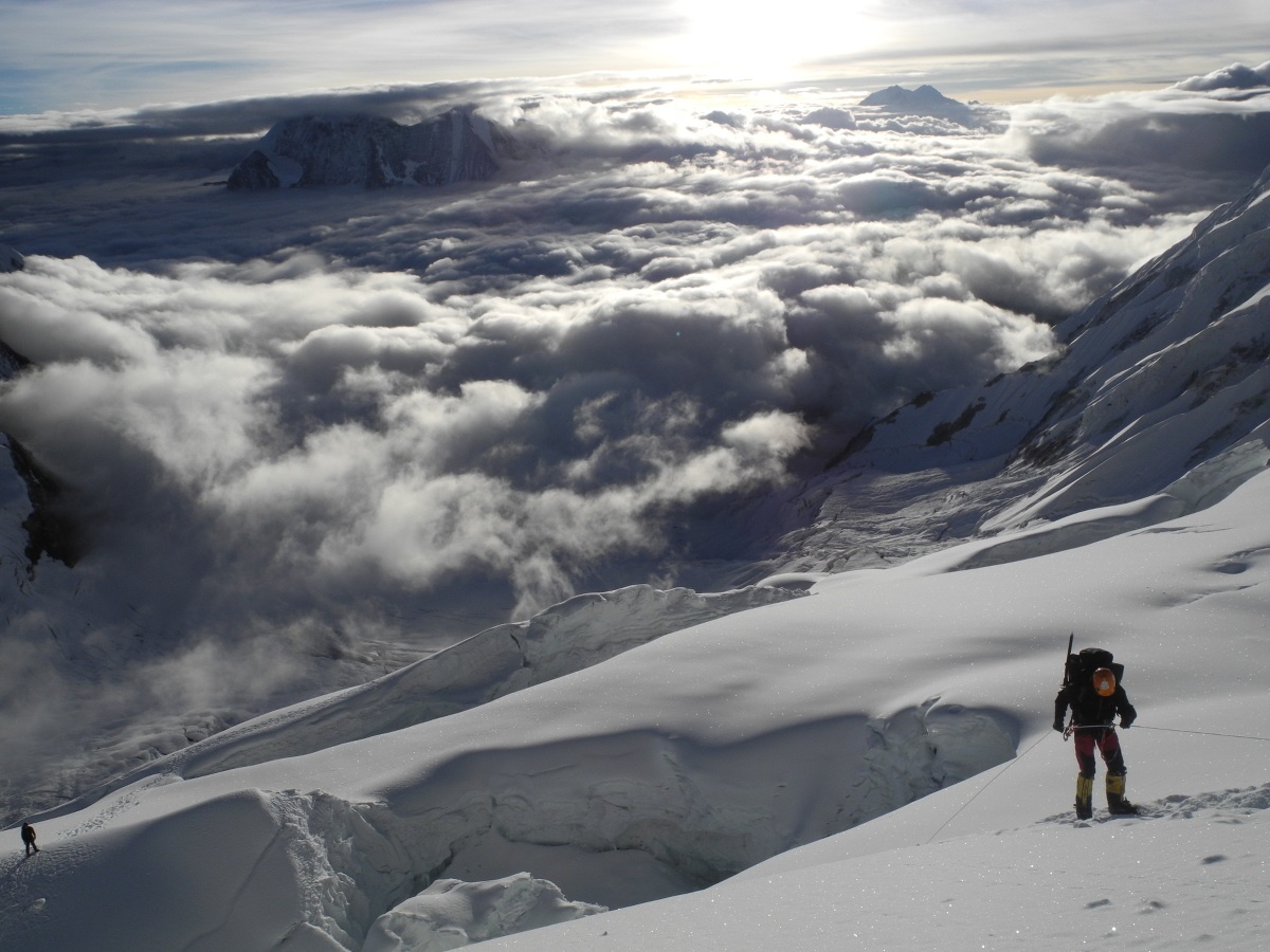 Woman mountaineering on a snowy slope high in the mountains with puffy white clouds