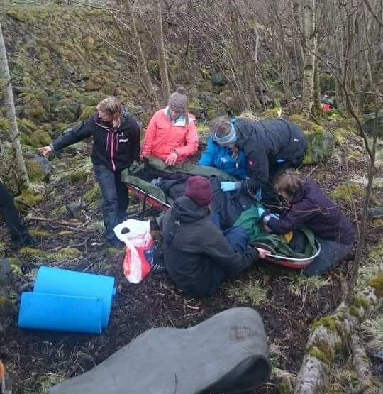 Five wilderness medicine students practice caring for a mock patient in a wooded area