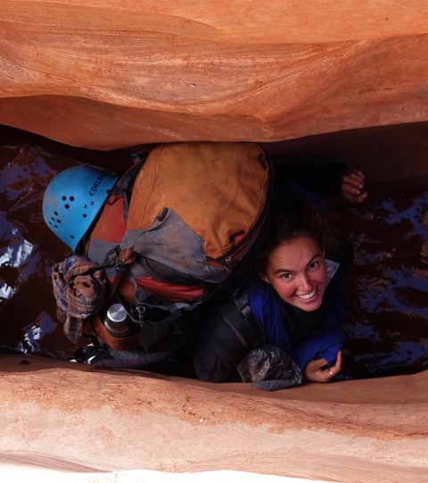 Exploring a canyon chimney wearing a backpack with climbing helmet attached