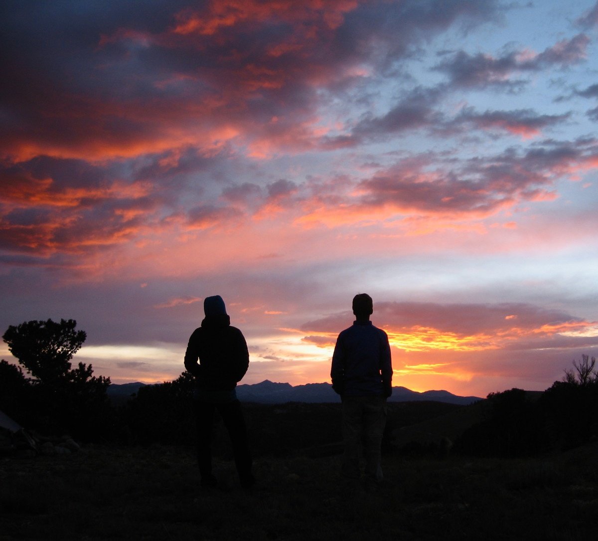 two silhouetted figures watch a dramatic sunset in the Rockies