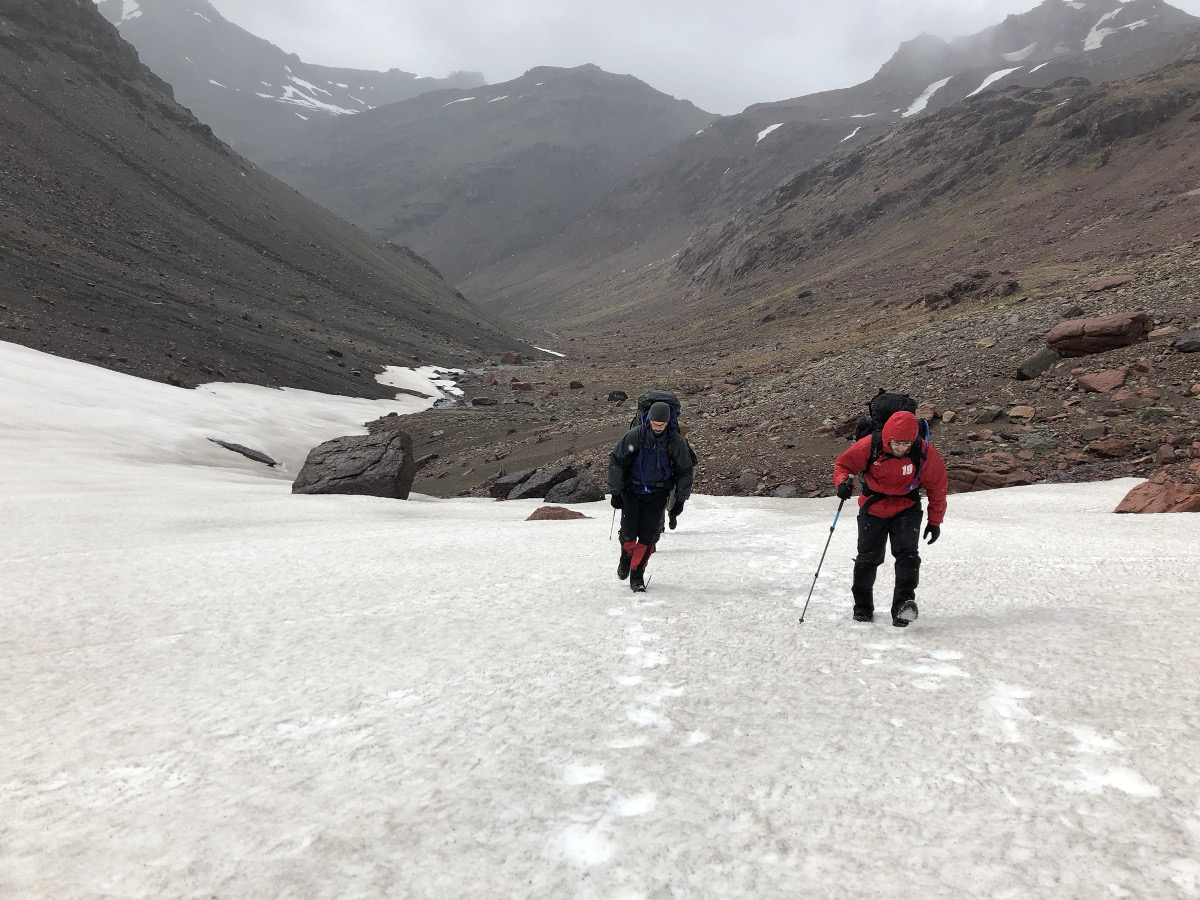 two students use trekking poles to ascend a steep snowfield