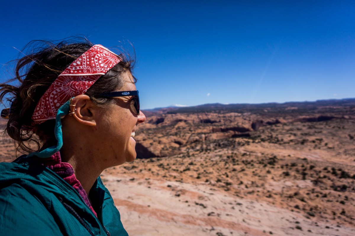 Woman wearing red bandana and sunglasses looks out at desert landscape on a sunny day