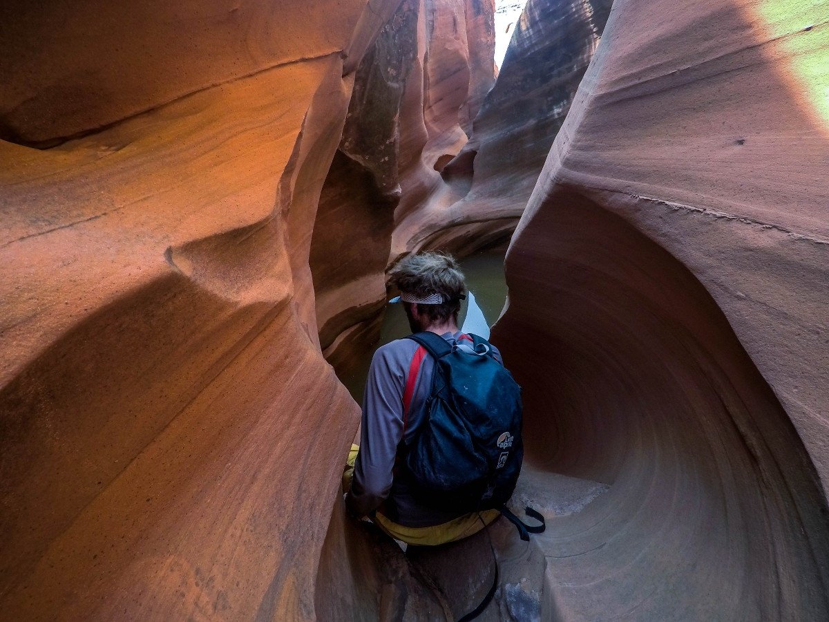 Student wearing a backpack squeezes through a slot canyon