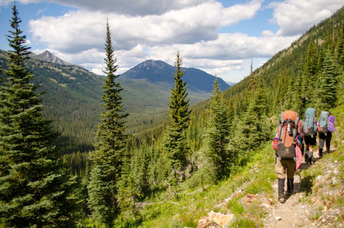 students wearing backpacks hike up a rocky trail single file in the mountains