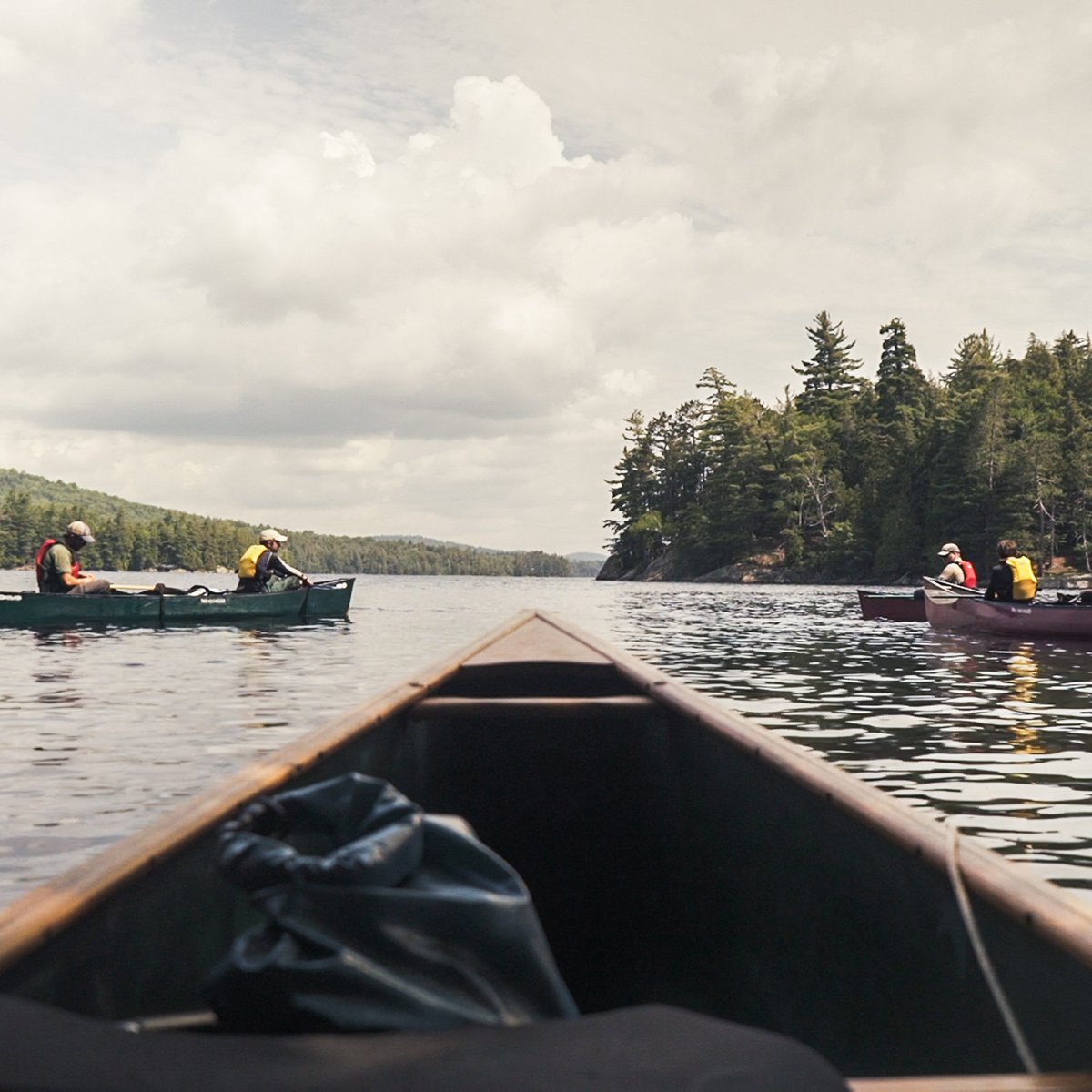 several canoes on calm lake in the Adirondacks as seen from the bow of a canoe