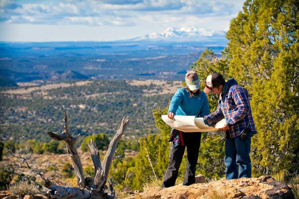 two people wearing baseball caps stand together to read a map