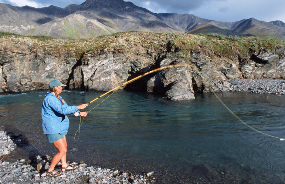 Woman wearing a hat fly fishes in a mountain lake on a sunny day