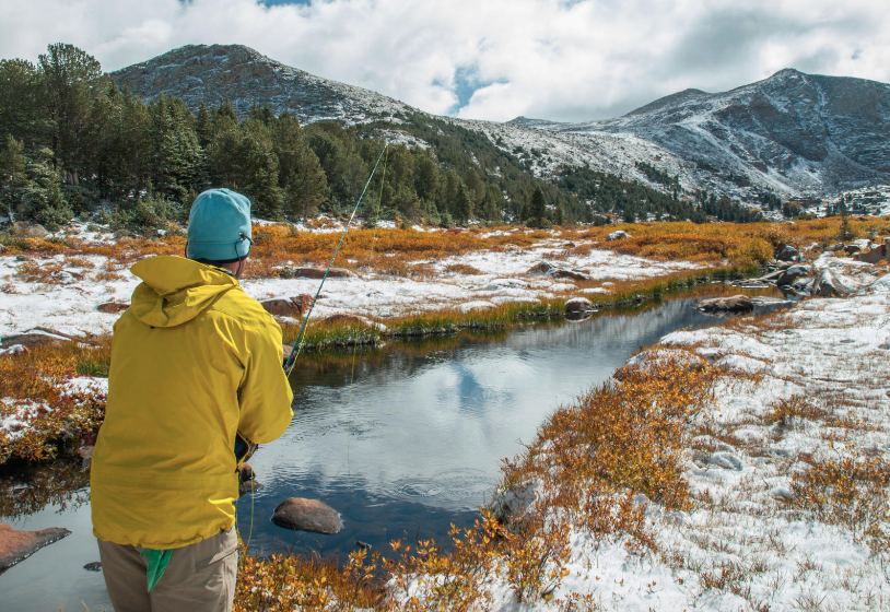 Person fishing on river in the mountains with snow on the banks