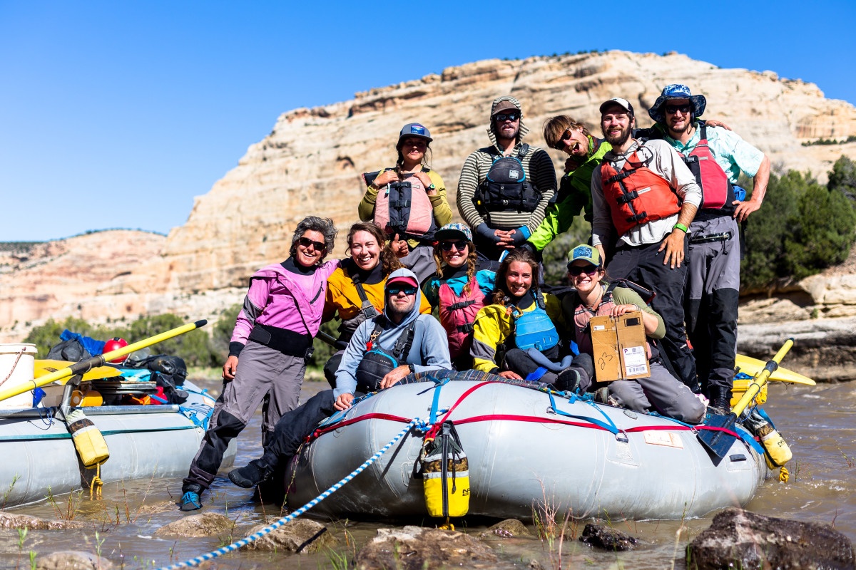 Smiling people pose for a group shot wearing river gear on a rafting expedition