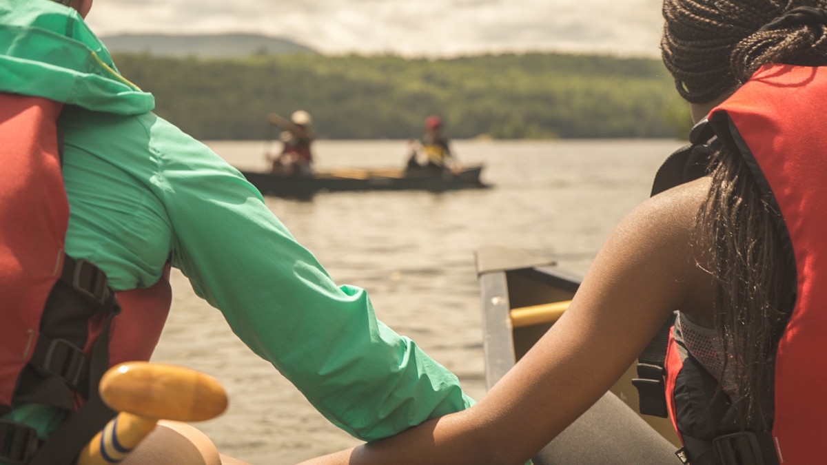 Two teen girls hold onto each other's canoe