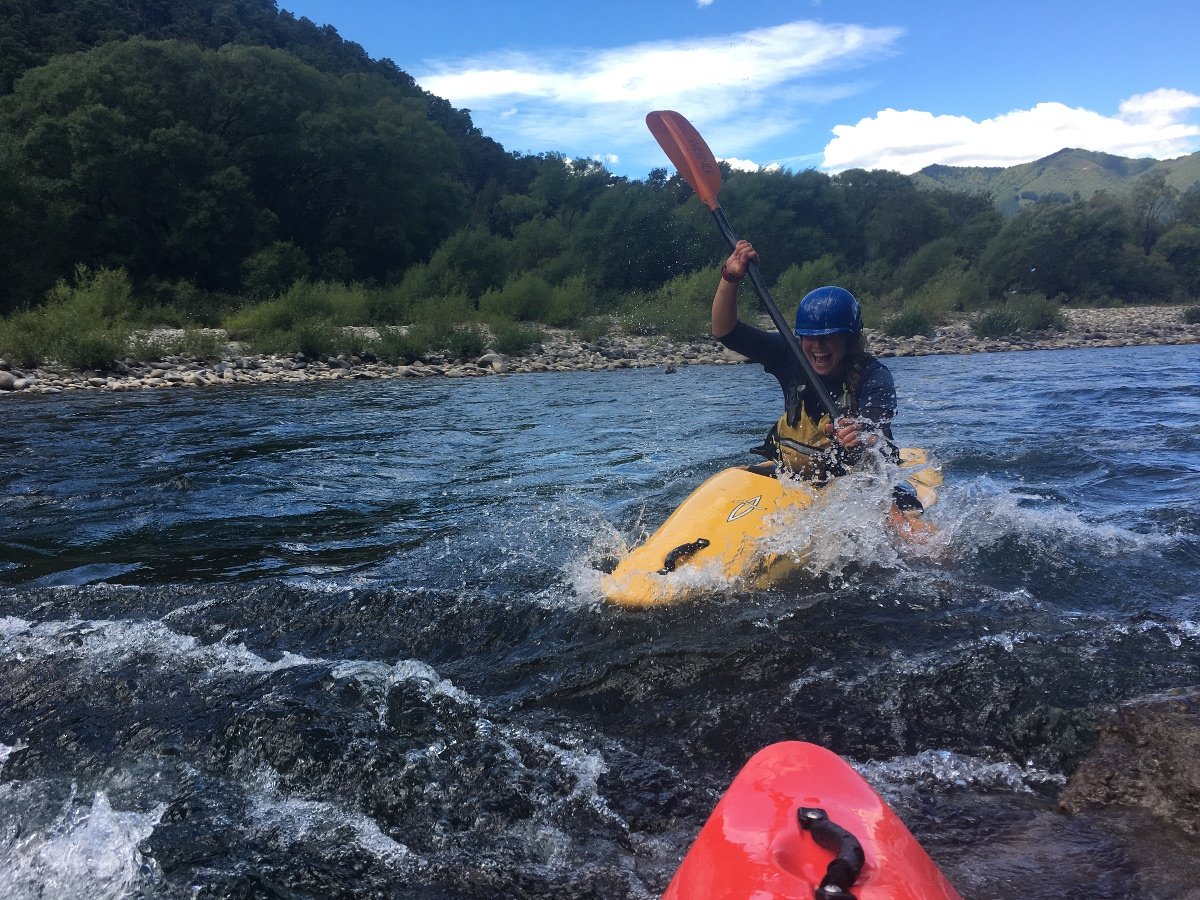 smiling woman wearing blue helmet paddles a yellow kayak on the river