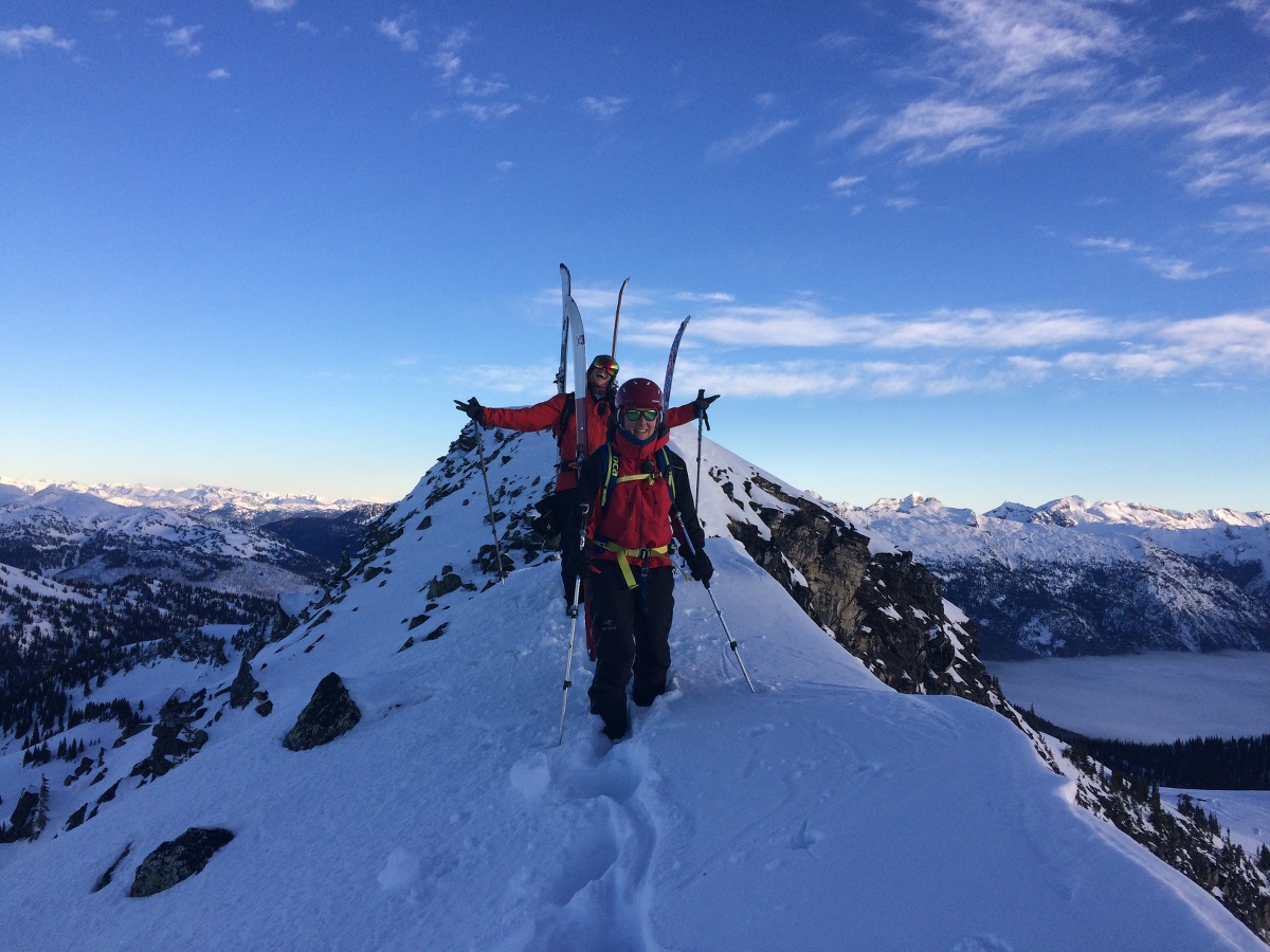 backcountry skiers move in single file at the top of a rocky peak covered in snow