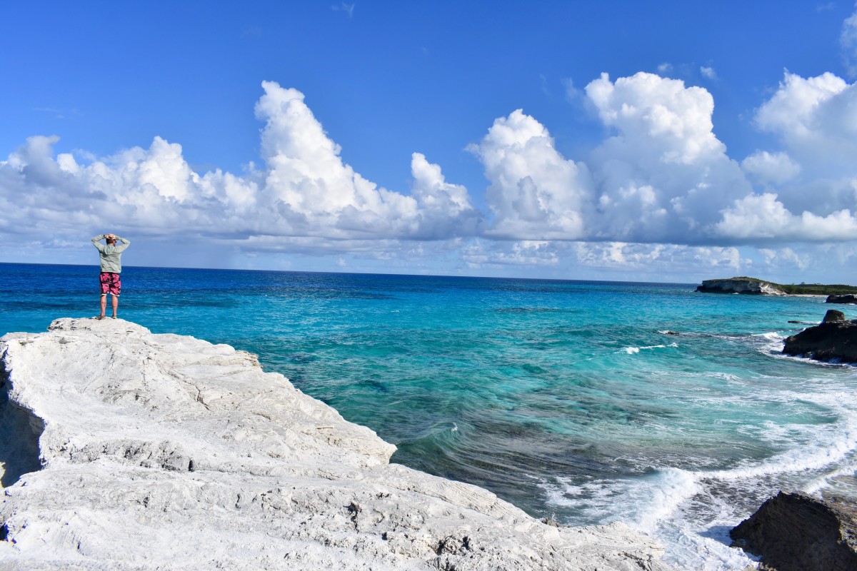 NOLS student stands on a rocky outcrop on the shore of the turquoise blue ocean in the Caribbean