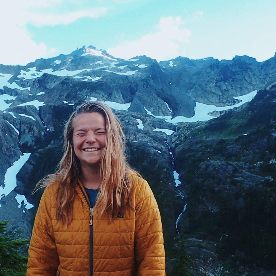 smiling NOLS backpacking student surrounded by mountains with patchy snow in the Pacific Northwest