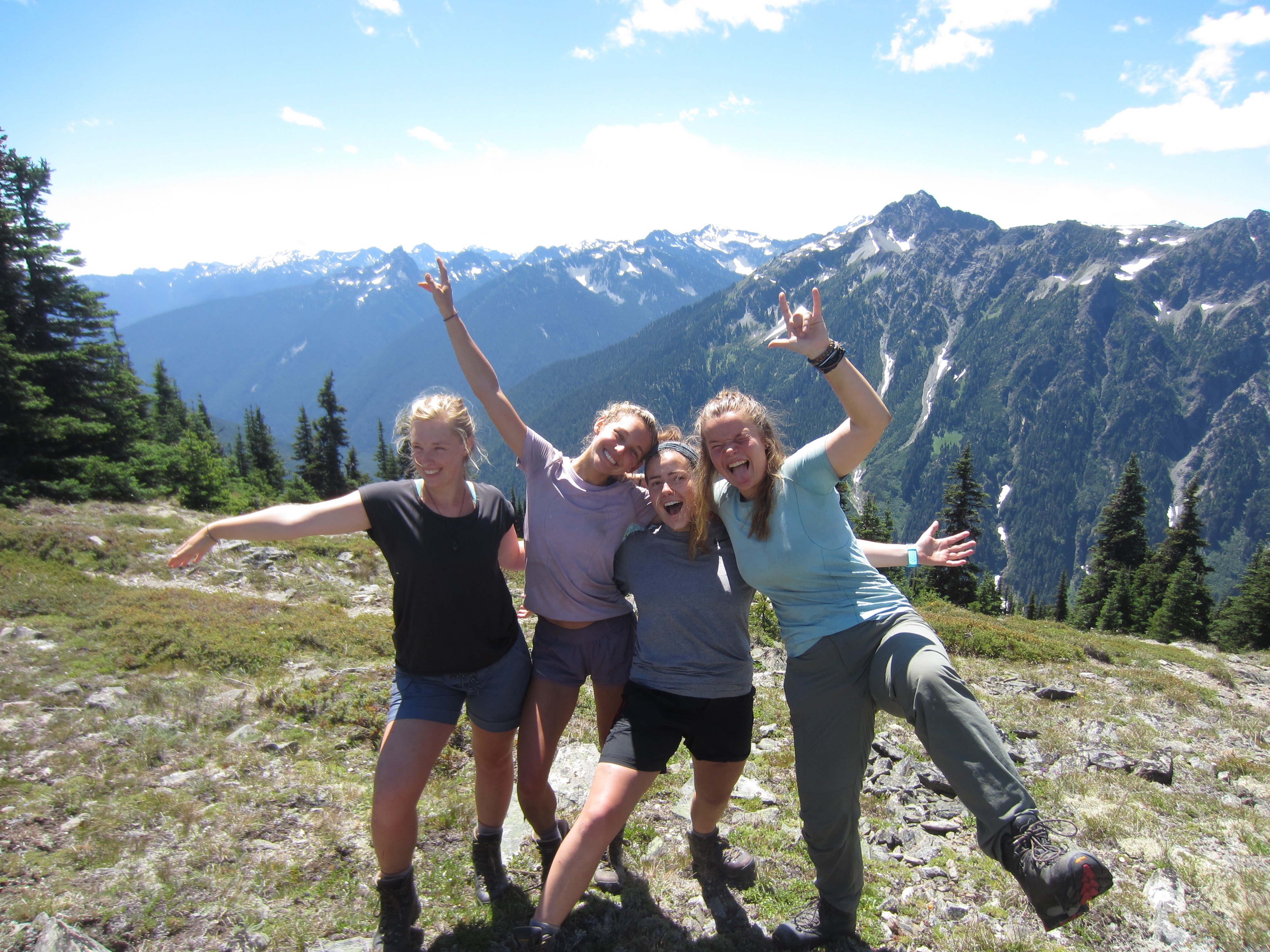 four NOLS students smile and celebrate reaching the top of Grey Wolf Pass in the Pacific Northwest together