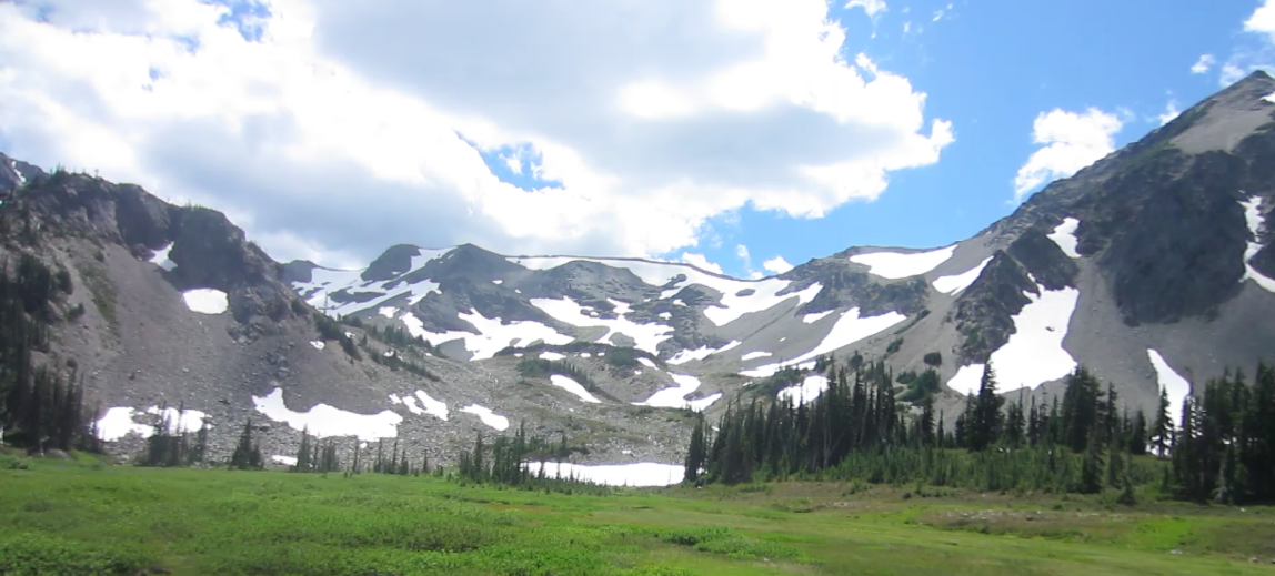 green valley leading up to a mountain pass dotted with snow in the Pacific Northwest