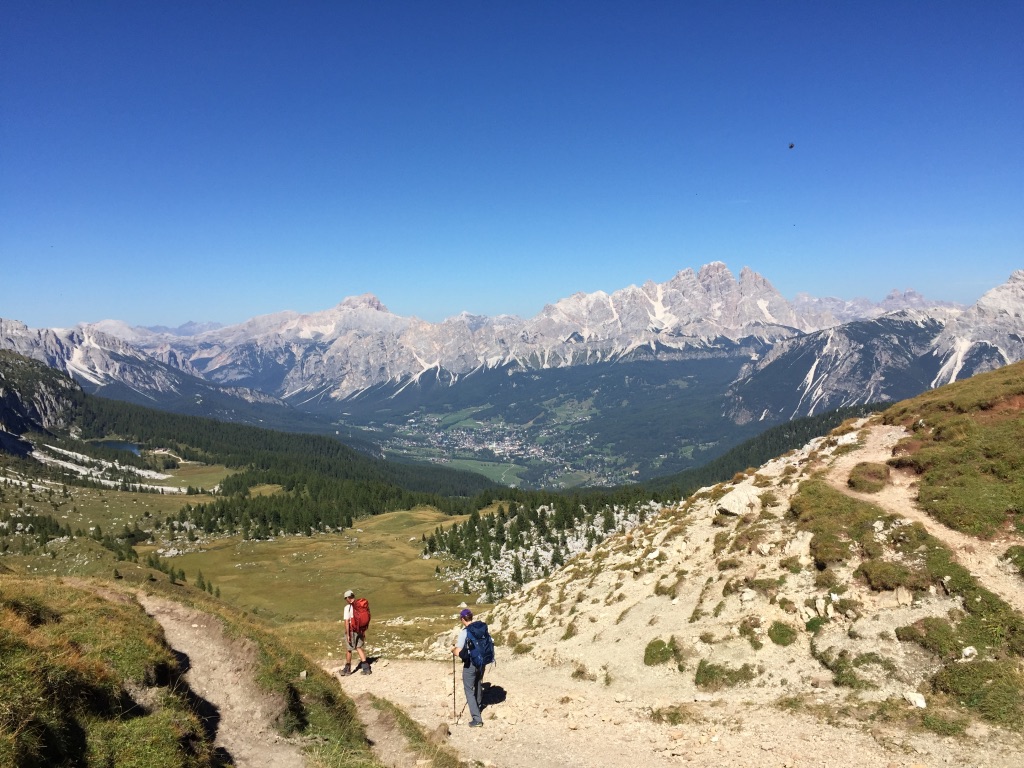 Two backpackers hike down a sandy trail in the mountains