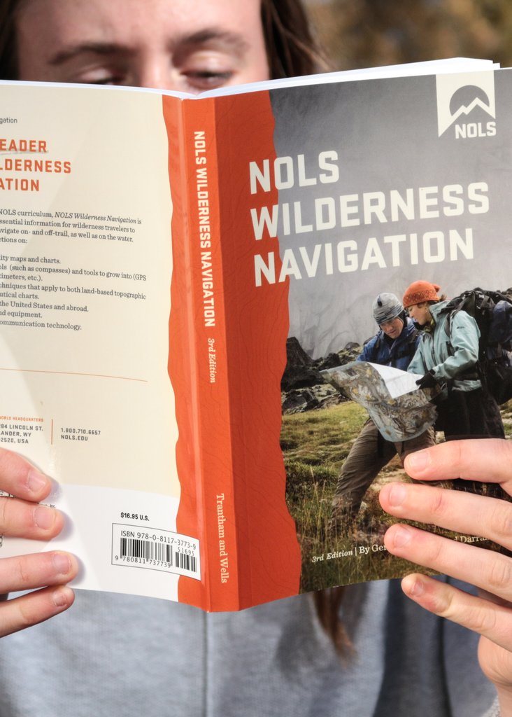 person holds NOLS Wilderness Navigation book