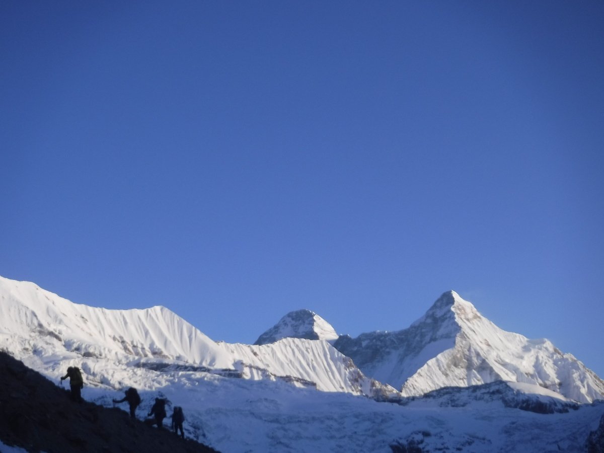 Students rope climb en route to Camp 1 on a cold, clear morning, with mountains Nanda Devi and Nanda Devi East in the background