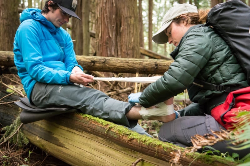 NOLS wilderness medicine student practices taping another student's ankle in the woods
