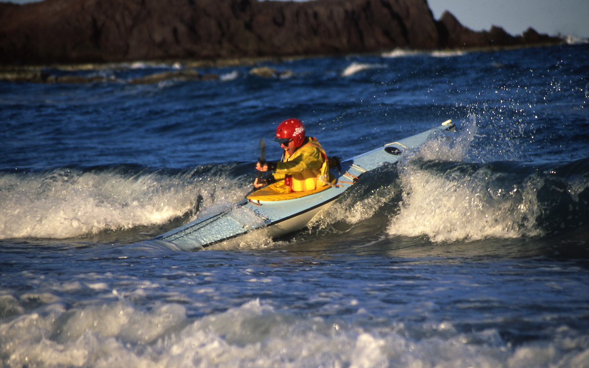 Smiling NOLS student paddles a sea kayak in the waves in Baja