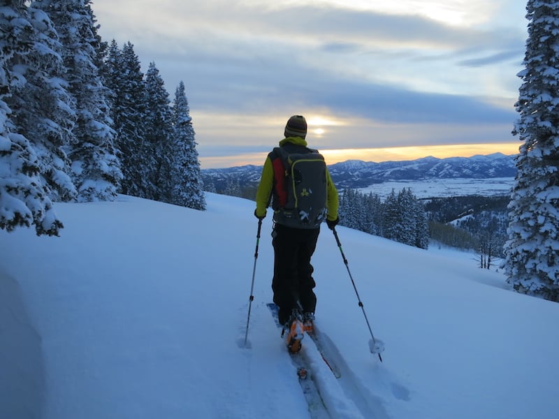 NOLS participant backcountry skis as the sun sets over snowy mountains