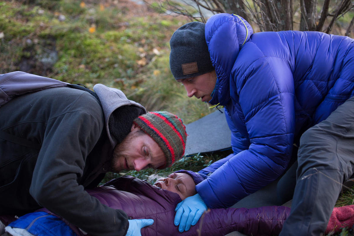 two NOLS Wilderness Medicine students bend over a patient in a practice scenario outdoors