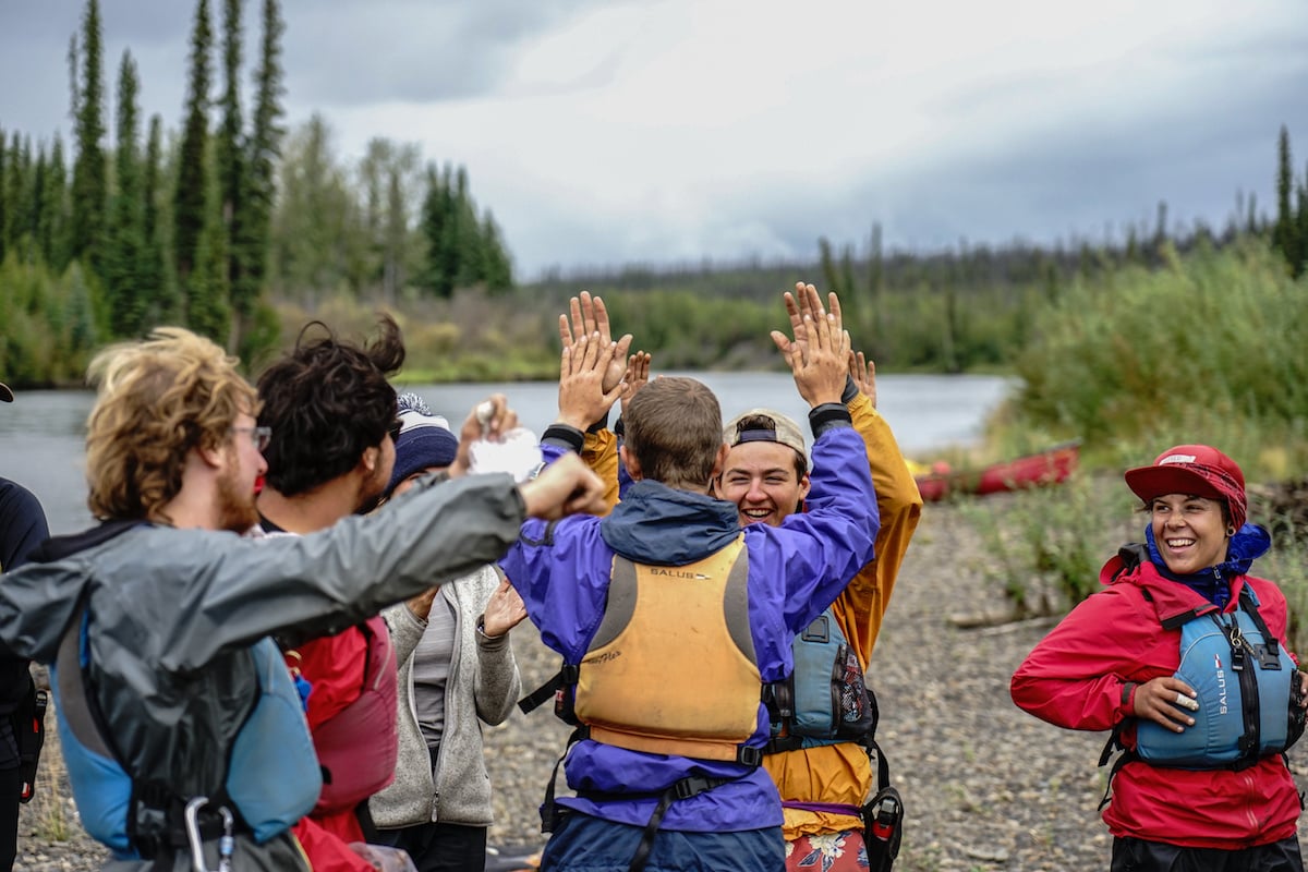 group of smiling NOLS students wearing river gear give each other high fives