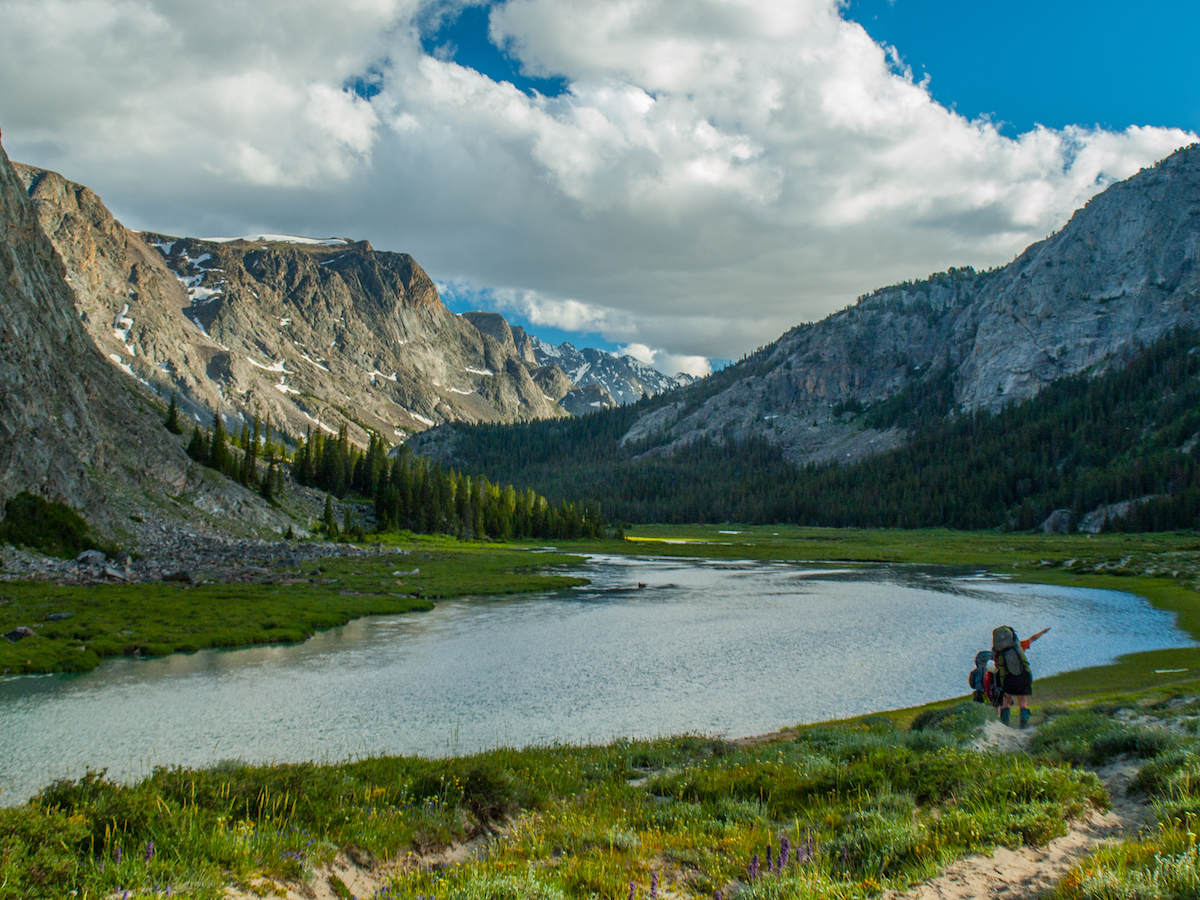 NOLS participants hike beside an alpine lake surrounded by rocky peaks in the Wind River Range