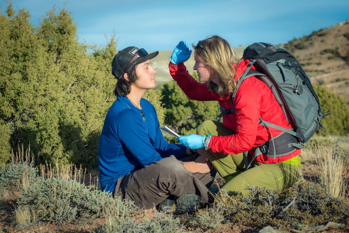 NOLS wilderness medicine student bends down beside a mock patient in the outdoors