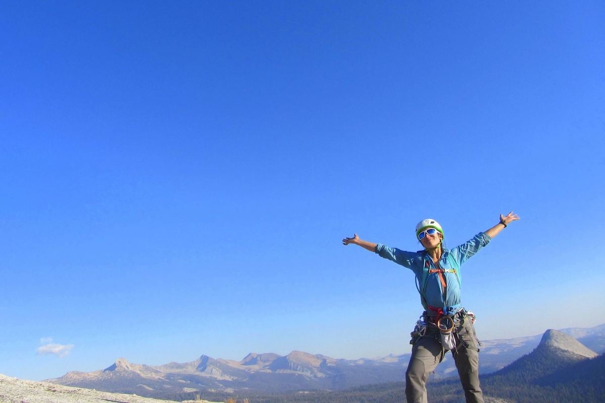 smiling NOLS instructor with arms outstretched on a beautiful day in the mountains