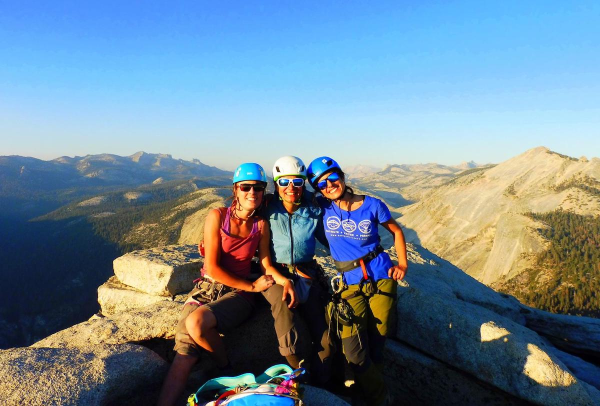 three female rock climbers smile for a group shot at Yosemite's half dome