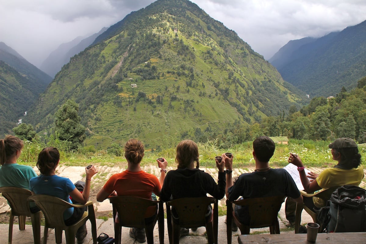 six NOLS students sit and enjoy chai and a view of the mountains while hiking in the Himalaya