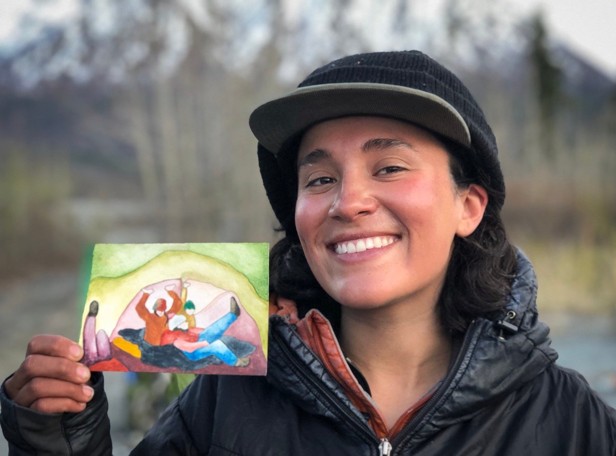 smiling NOLS participant on a women's mountaineering seminar holds up a watercolor painting 