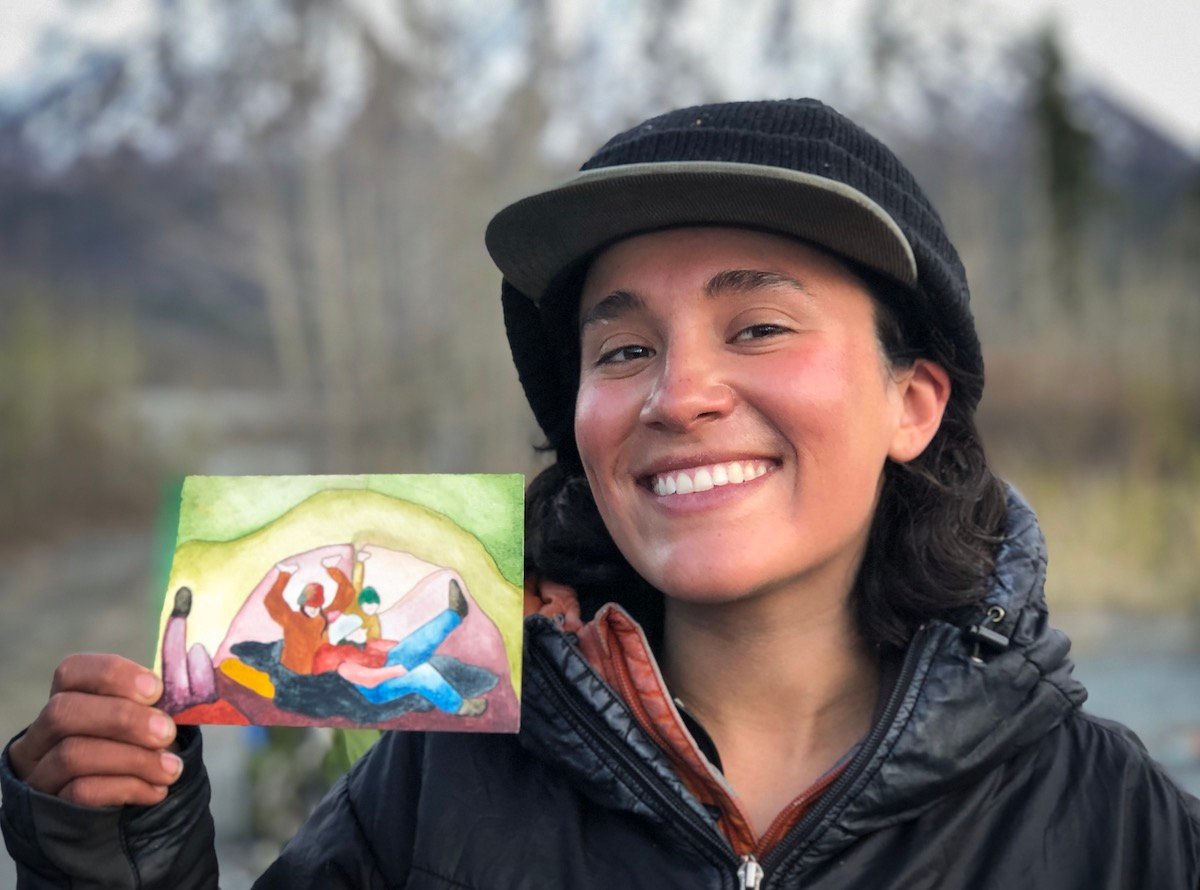 smiling NOLS participant on a women's mountaineering seminar holds up a watercolor painting