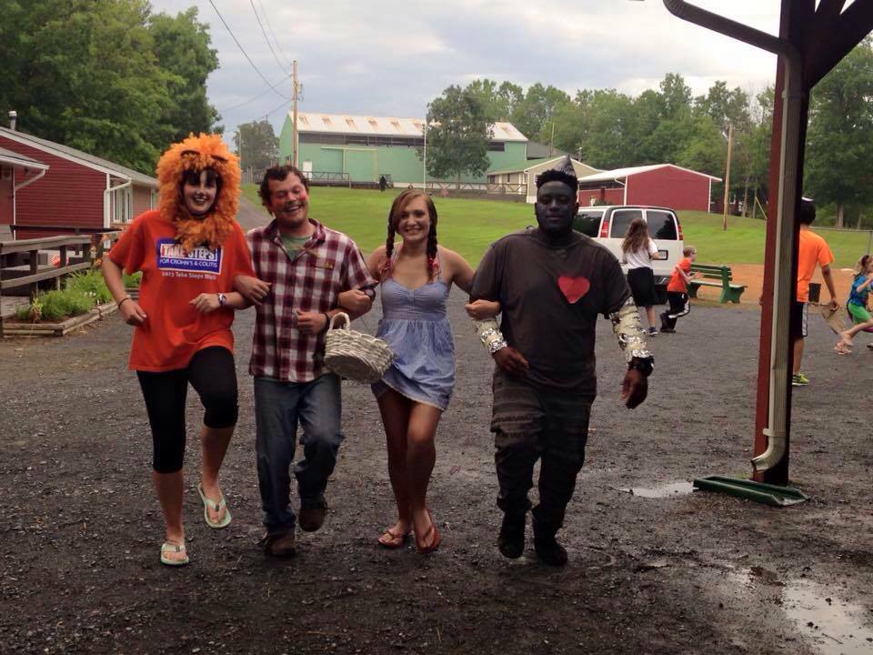 Four people dressed as the Lion, Scarecrow, Dorothy, and the Tin Man from the Wizard of Oz. They skip down a path