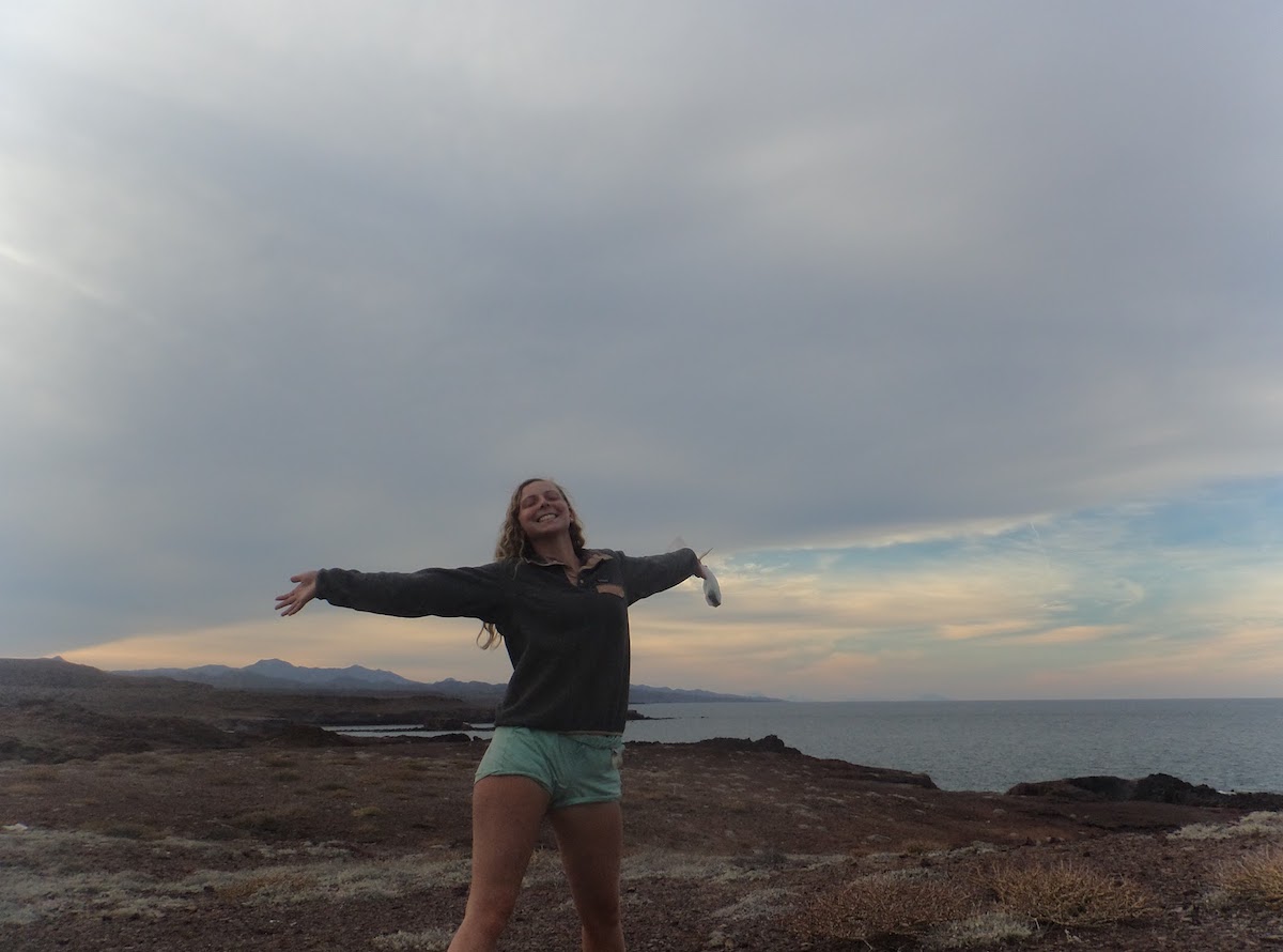 smiling NOLS student with arms outstretched on Baja coast