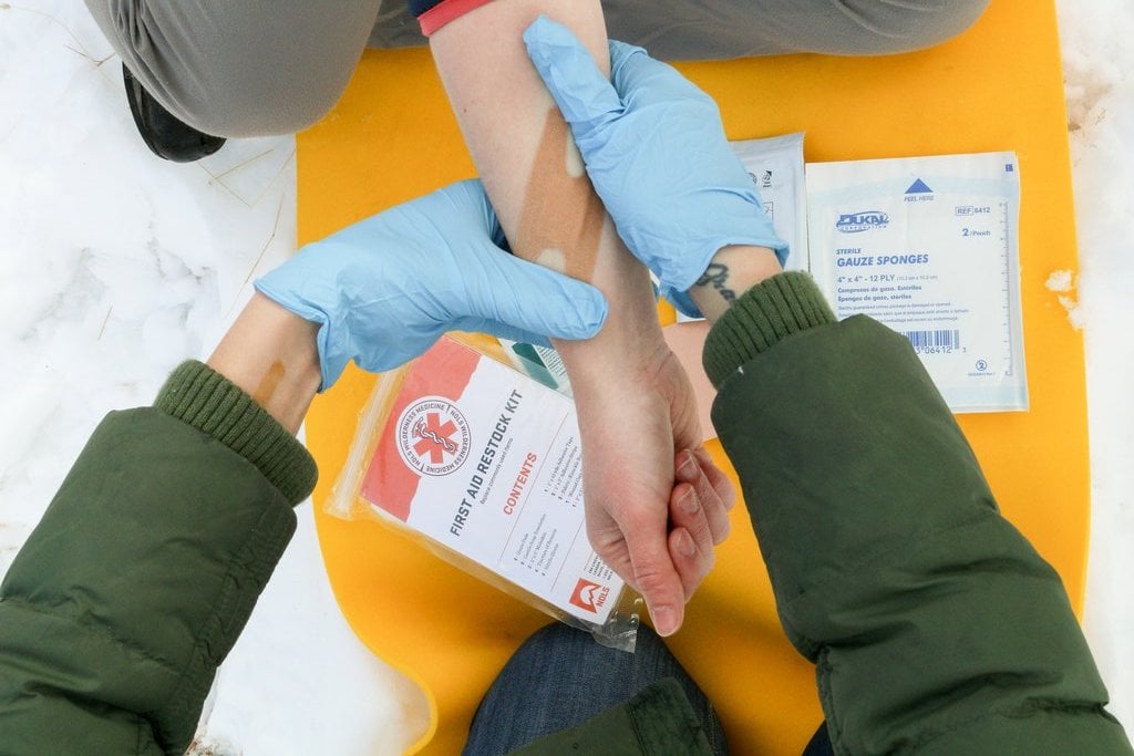 close-up of gloved hands applying a bandage during a NOLS scenario