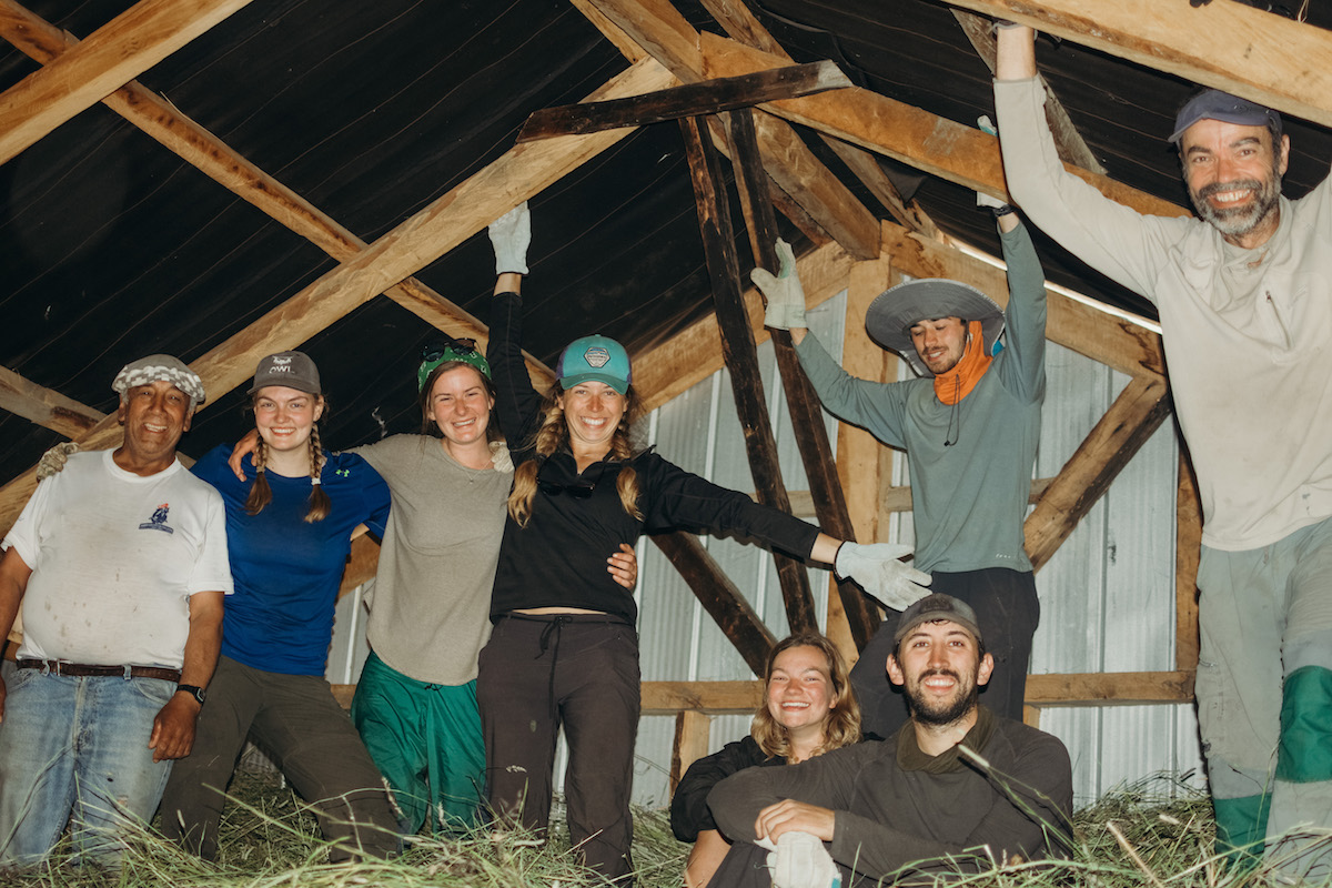 eight smiling people standing in hay in a barn in Patagonia