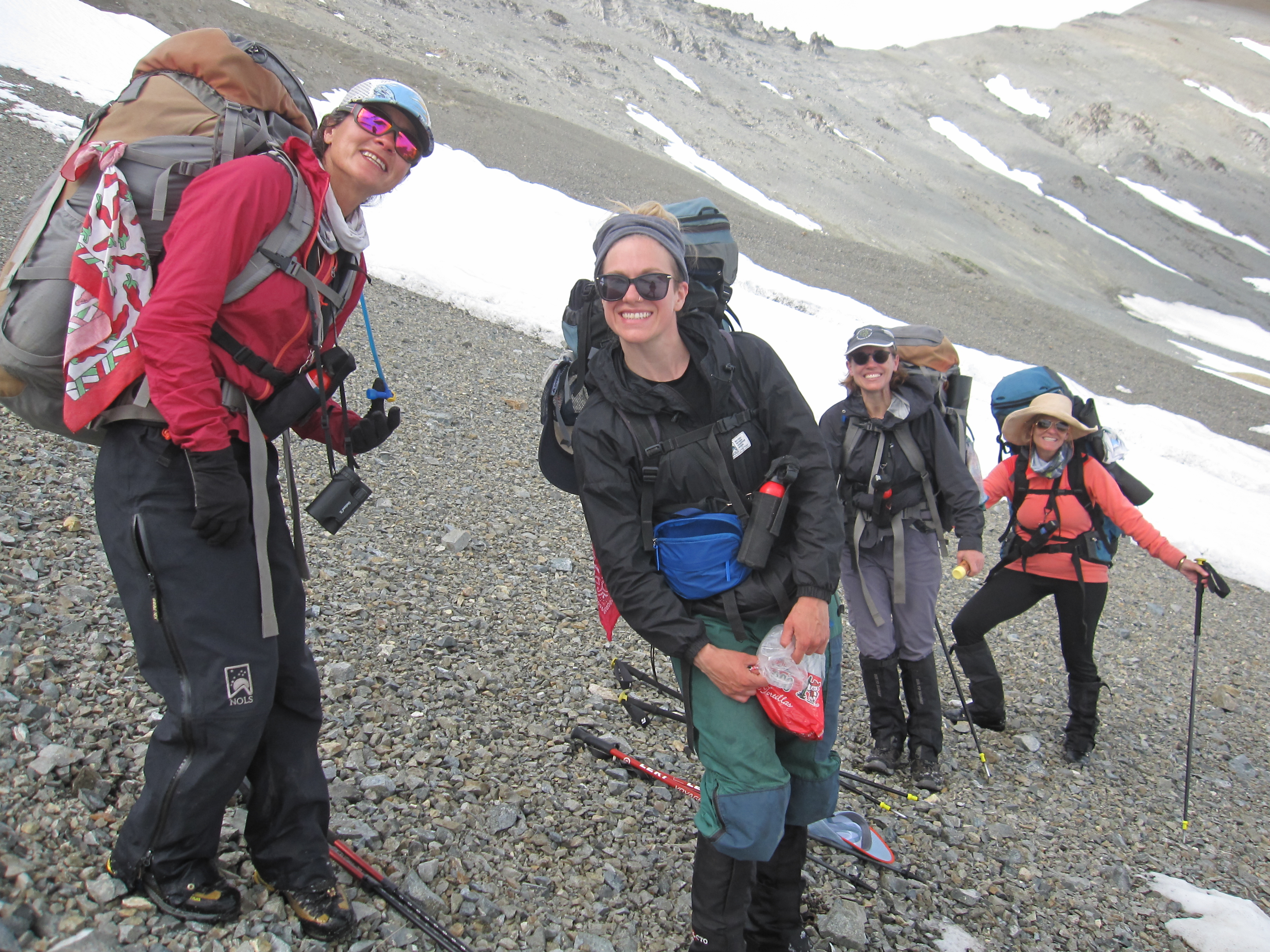 smiling women on a NOLS backpacking course pause on a scree slope in Alaska