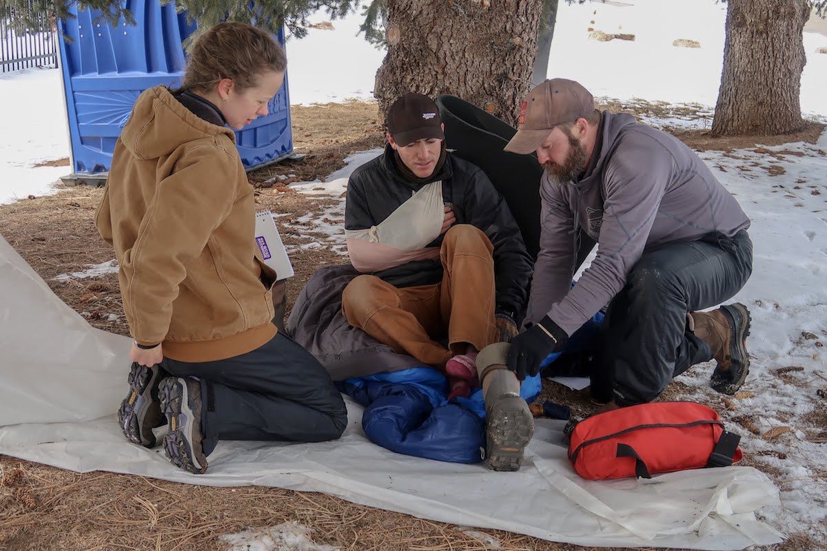 3 NOLS students do a patient assessment of a person with a mock arm injury