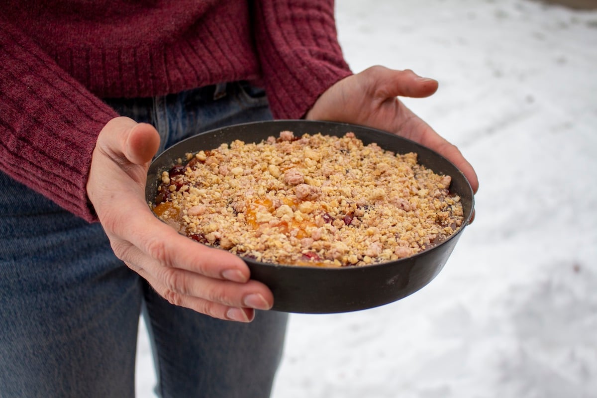 person wearing red sweater and jeans holds backcountry fruit pie