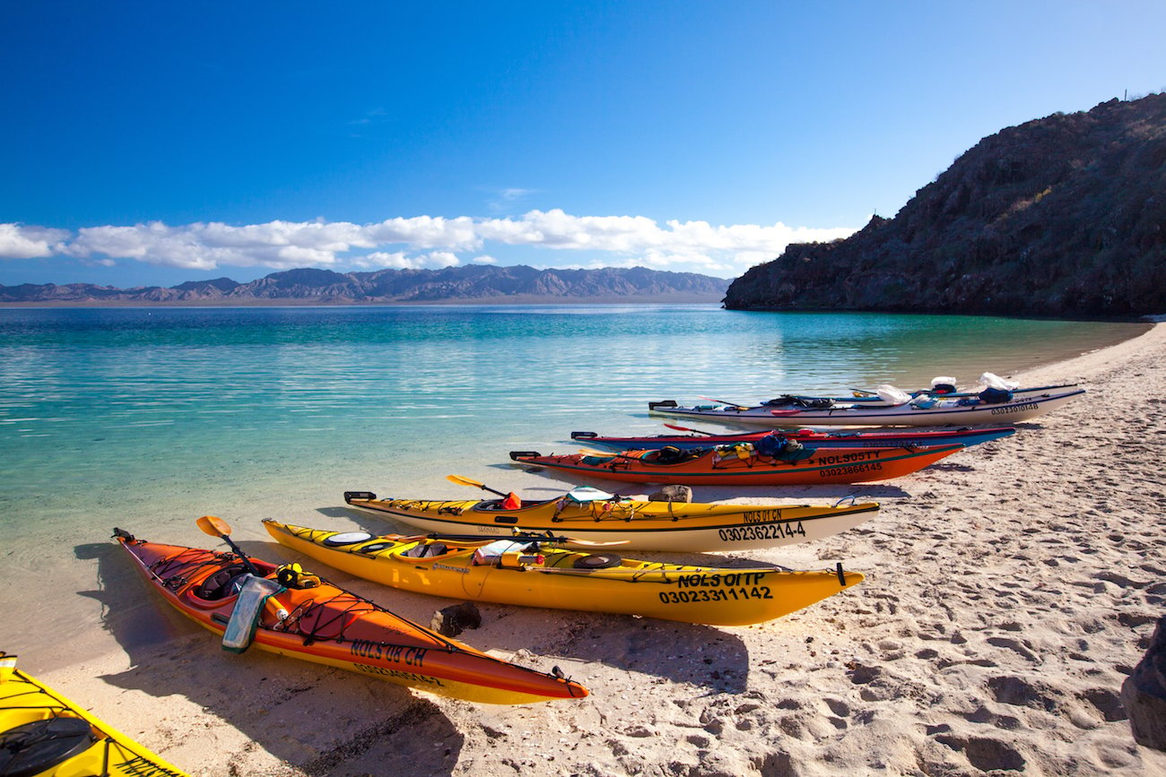 NOLS kayaks on a sandy beach in Baja with turquoise water and coastal mountains