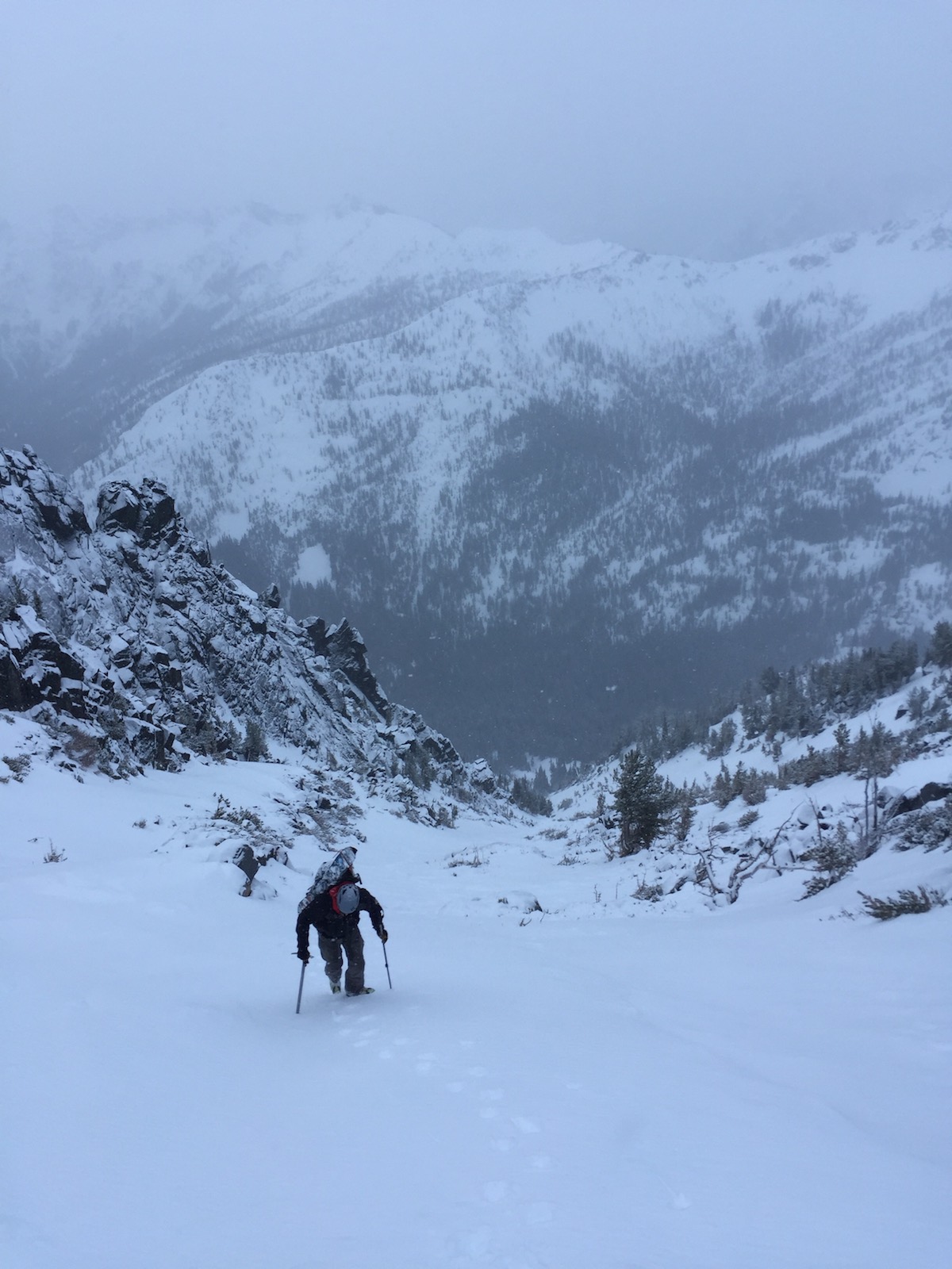 Skier climbing up a couloir using poles on a snowy day