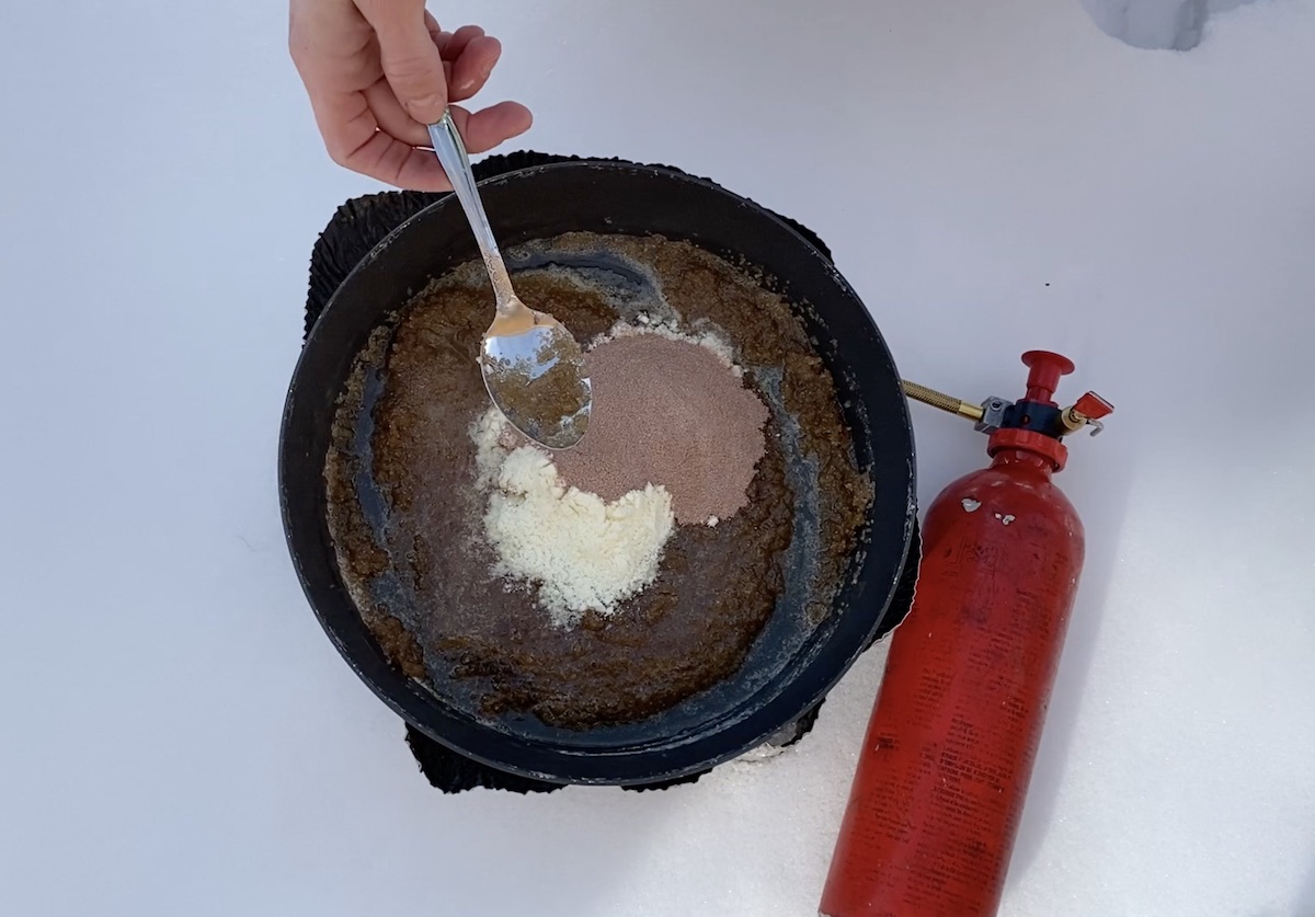 using a spoon to stir cocoa and powdered milk into no-bake cookie batter on a campstove