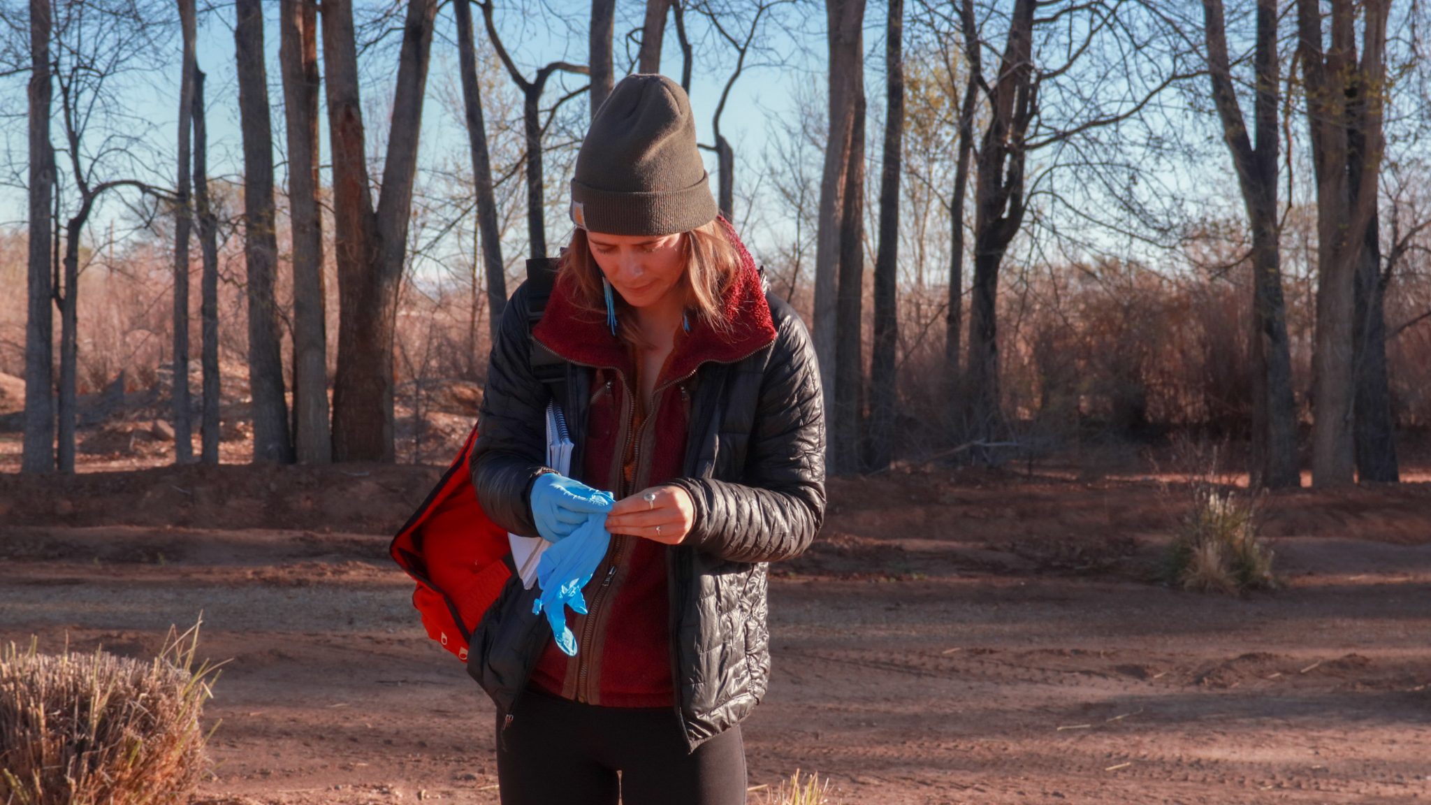 Woman in woods surrounded by dead trees putting gloves on