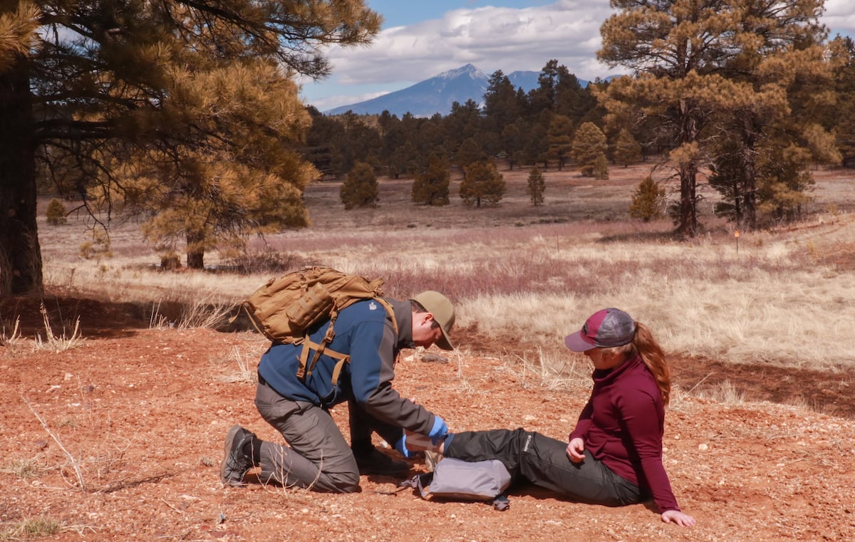 NOLS Wilderness Medicine practices splinting a patient's leg with mountains in the distance
