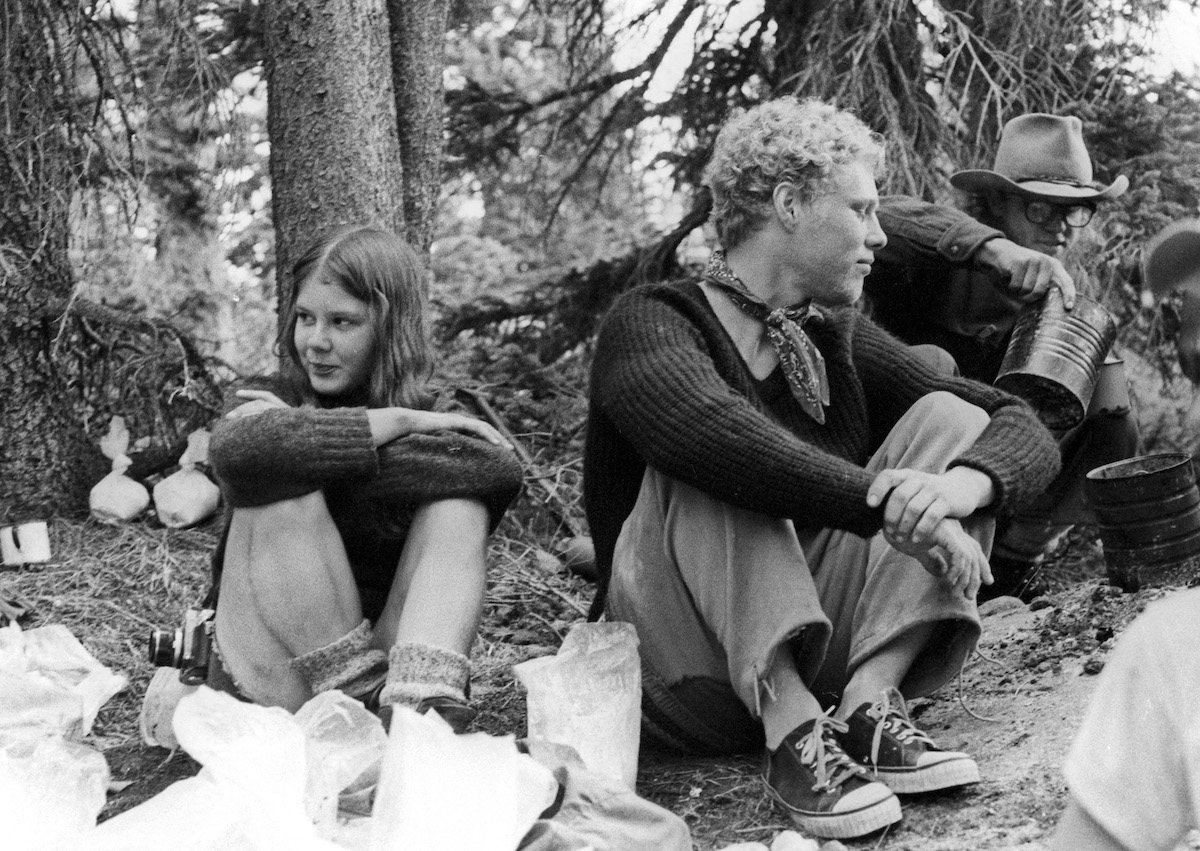 black and white photo of several NOLS students taking a break on an expedition in the 1970s with one student pouring liquid out of a billycan