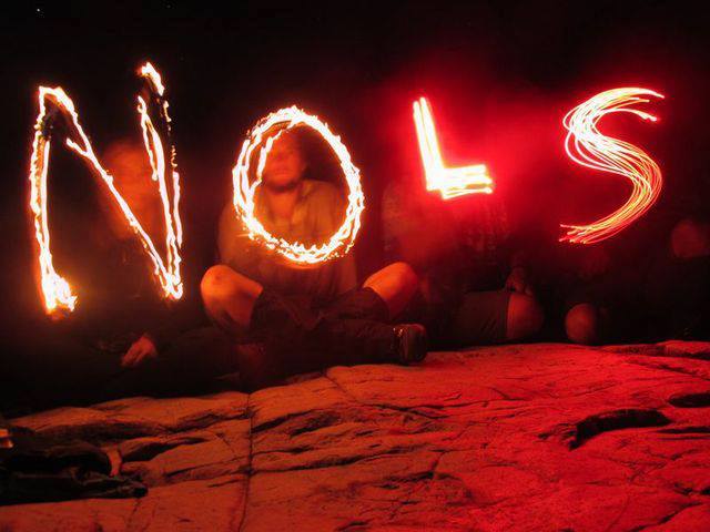 Four students sit on a rock in the dark and spell NOLS with glow sticks